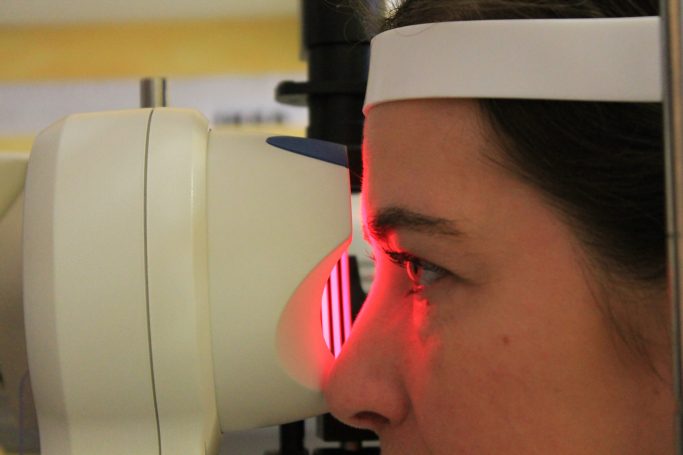 Persona realizando una prueba ocular con un topógrafo, instrumento óptico que emite circunferencias de luz roja.