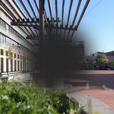 Representación de la visión con DMAE Imagen de una plaza de ciudad con una mancha oscura central y visión borrosa, simulando la visión de la DMAE.