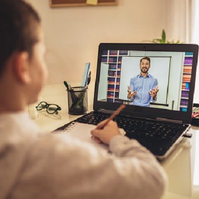 Maestros Niño tomando apuntes mientras sigue una clase por videoconferencia en su ordenador.