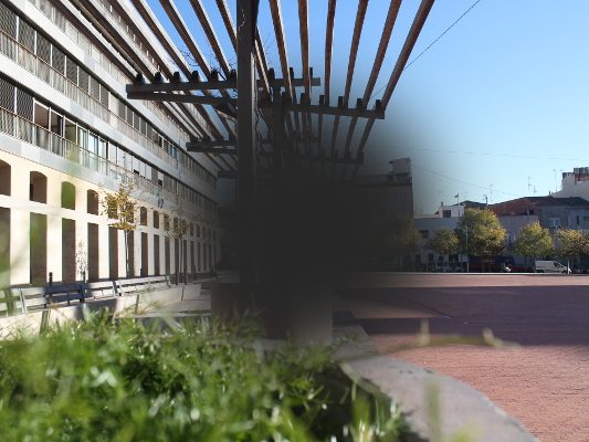 Representación de la visión con DMAE. Imagen de una plaza de ciudad con una mancha oscura central y visión borrosa, simulando la visión de la DMAE.