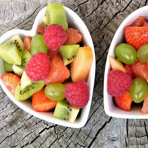 Nutricionistas Ensaladas de frutas en tazones con forma de corazón, mezclando fresas, kiwis y uvas.